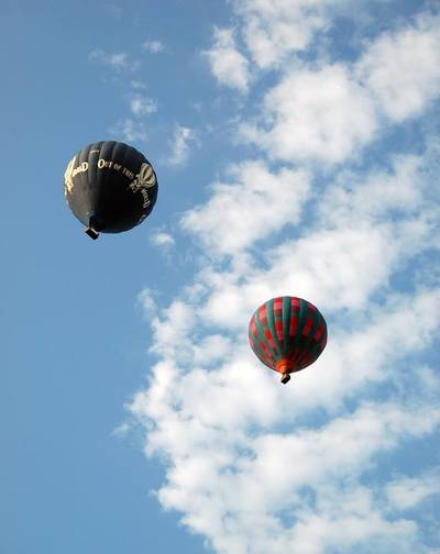 Blue sky, fluffy clouds and two hot air balloons, seen from below